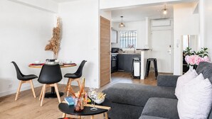 Ein modernes Wohnzimmer mit grauem Sofa, schwarzen Stühlen, einem Esstisch mit einer Vase getrockneter Pflanzen und einer im Hintergrund sichtbaren Küche.
