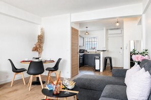 A modern living room with a grey sofa, black chairs, a dining table with a vase of dried plants, and a kitchen visible in the background. - 2 Bedrooms Antibes Center, Balcony, Antibes, France (Antibes)