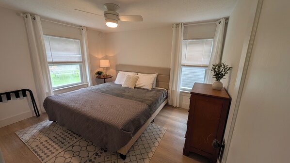 A bedroom with a bed, bedside tables, a nightstand, a ceiling fan, and a window with curtains.