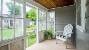 Ein überdachter Balkon mit großen Fenstern, einem weißen Adirondack-Sessel und einem Blumentopf.