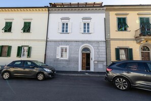 A row of three-story buildings with a central door and windows, parked cars, and a clear sky.