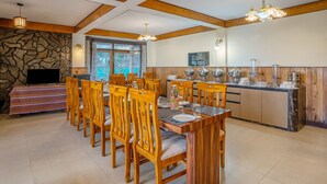 A dining area with wooden chairs and a table, a kitchen with buffet setup, stone wall, and wooden ceiling beams. - Treebo Eeshan Rodhi Resort, Darjeeling (Darjeeling)