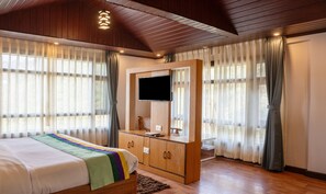 A bedroom with a bed, a TV mounted on a wooden cabinet, and large windows with curtains. - Treebo Eeshan Rodhi Resort, Darjeeling (Darjeeling)