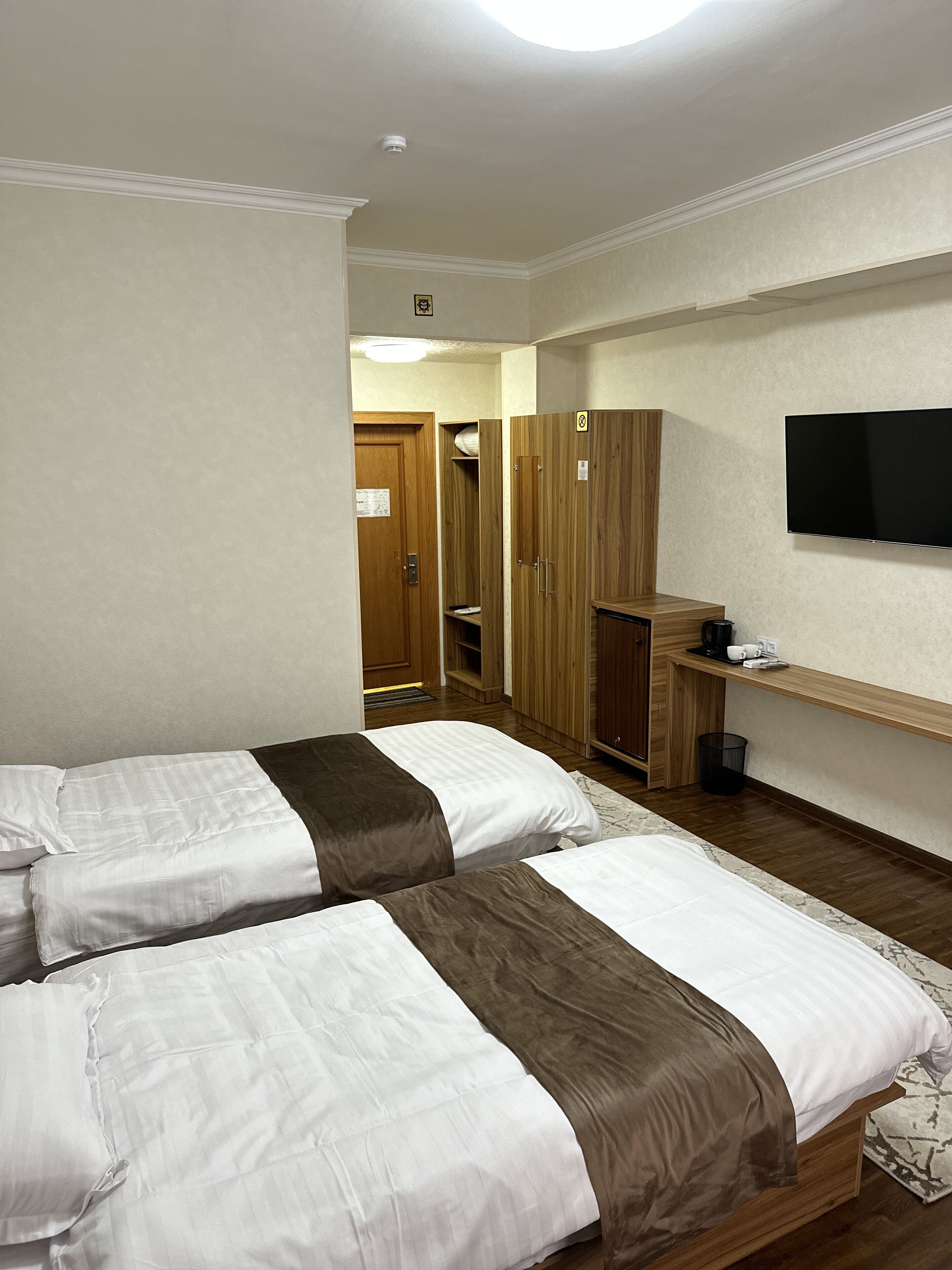Une chambre d’hôtel avec deux lits, un téléviseur fixé au mur et une armoire en bois.