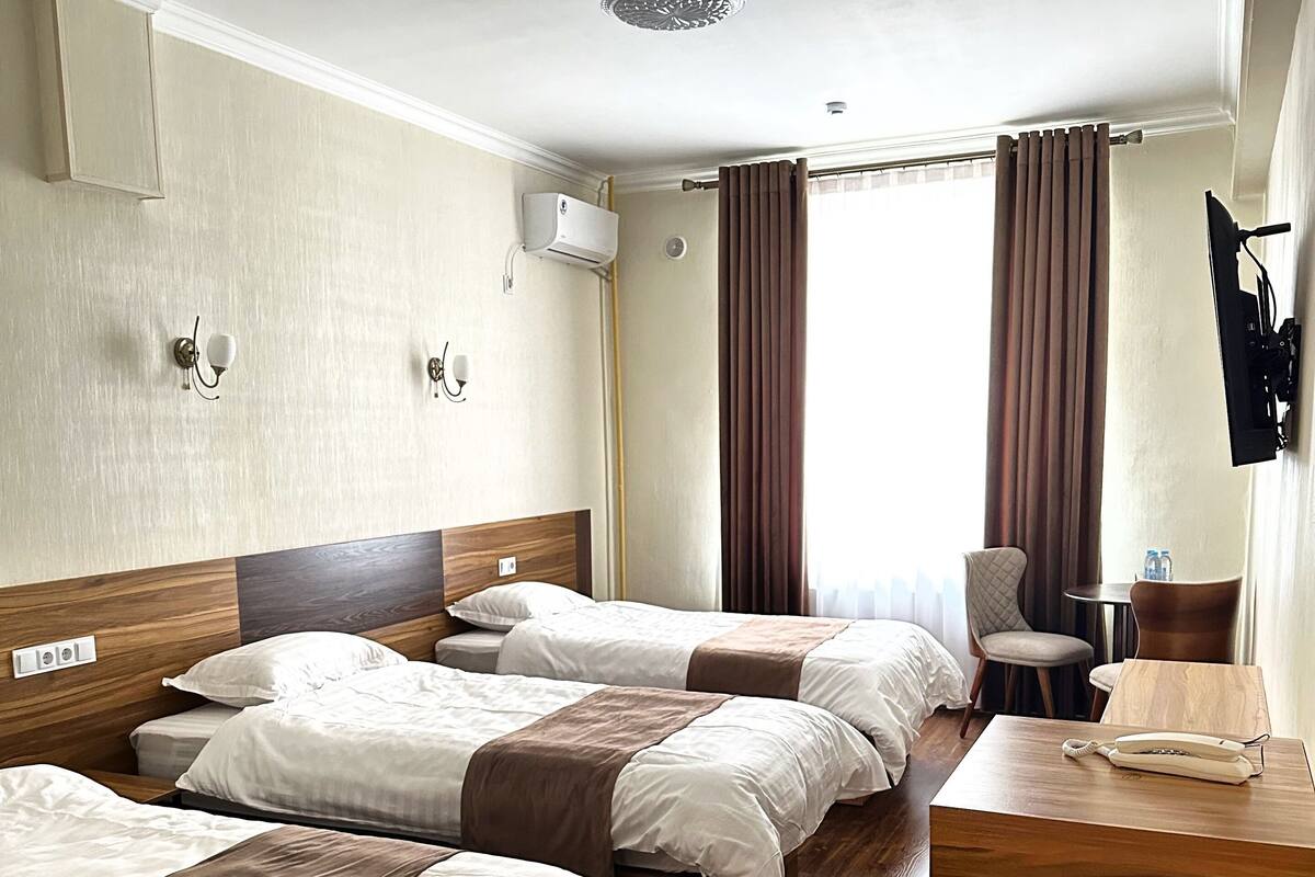 A hotel room with three beds, a wooden dresser, a desk with a phone, and a chair.
