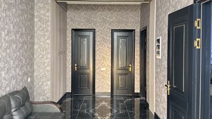 A hallway with a black leather sofa, two doors with gold handles, and a marble floor. - Colibri Hotel  (Bukhara)