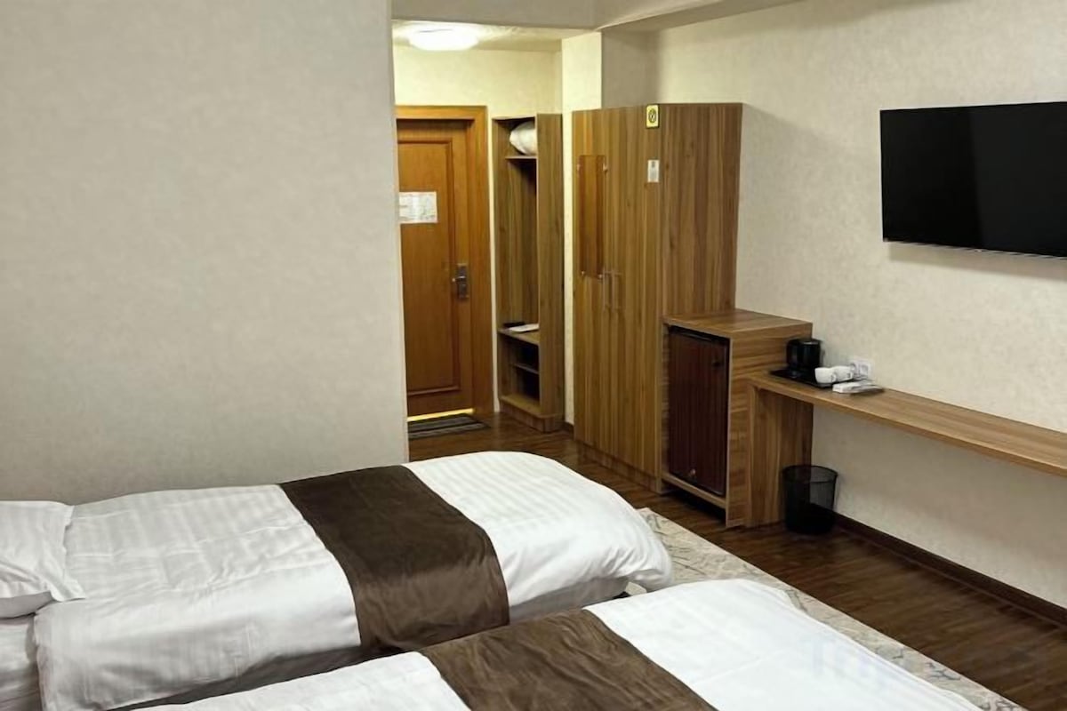 Une chambre d’hôtel avec deux lits, une télévision, une armoire et une petite table avec une machine à café.