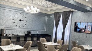 A modern dining area with multiple tables and chairs, a large wall clock, and a television screen. - Colibri Hotel  (Bukhara)