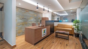 Un espace d’accueil comprenant un comptoir de réception en bois, un canapé en cuir, une plante en pot et un mur en pierre.