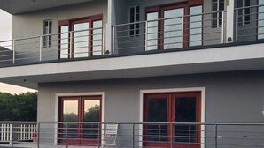Un edificio moderno de dos pisos con balcón, piscina con iluminación azul y una puerta roja.