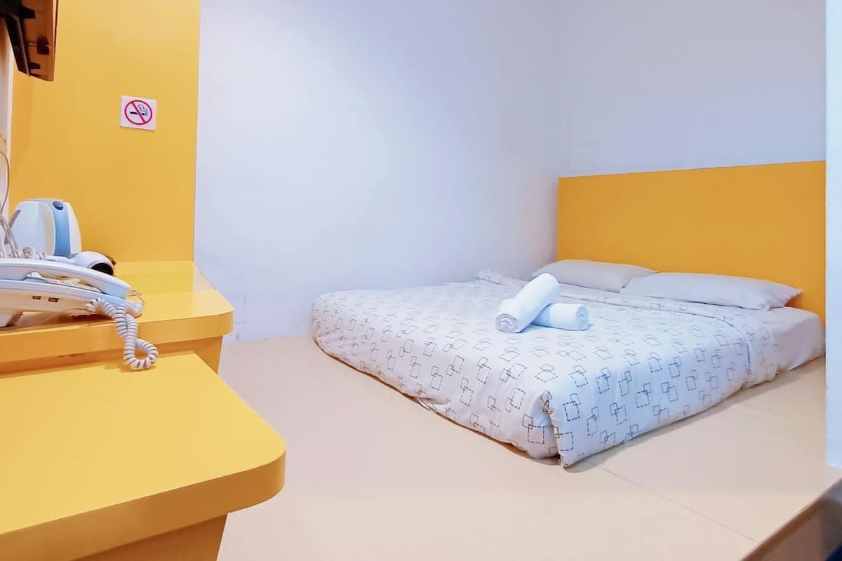 Une petite pièce, bien éclairée, avec un lit, un bureau doté d’un téléphone et un panneau « interdiction de fumer » accroché au mur.
