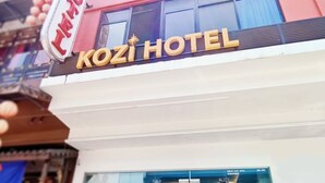 Une enseigne d’hôtel avec l’inscription « KOZI HOTEL » en lettres dorées sur un fond blanc.
