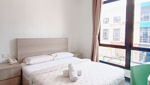 Une chambre d’hôtel équipée d’un lit, d’une table de chevet, d’un téléphone et offrant une vue sur l’extérieur grâce à de grandes fenêtres.