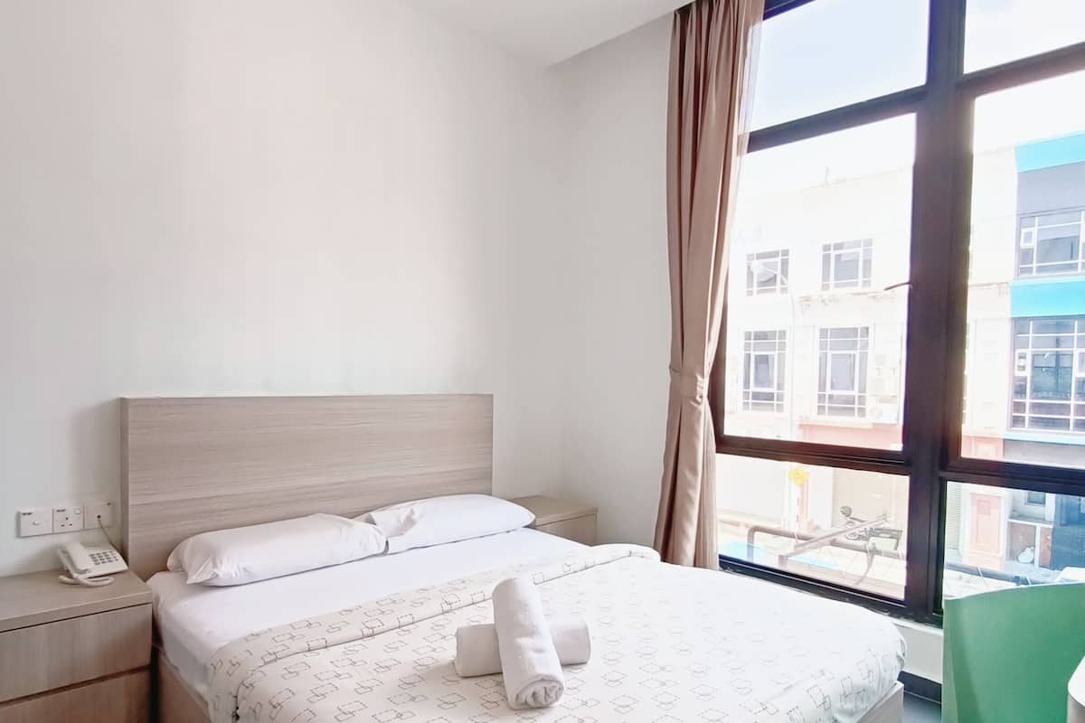 Une chambre d’hôtel équipée d’un lit, d’une table de chevet, d’un téléphone et offrant une vue sur l’extérieur grâce à de grandes fenêtres.