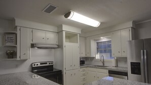 A kitchen with white cabinets, a stainless steel refrigerator, a built-in oven, and a window with blinds. - A Quiet Place - Dogwood Retreat in Texarkana (Texarkana)