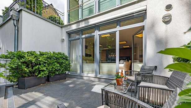 A patio with wicker furniture, a glass table, and potted plants.