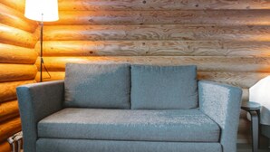 A log cabin interior with a grey upholstered armchair, a floor lamp, and a small table. - Rustholli 9 by Interhome (Tampere)