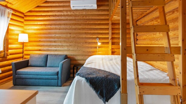 A cozy log cabin room with a wooden ladder, a bed, a sofa, and a lamp. - Rustholli 9 by Interhome (Tampere)