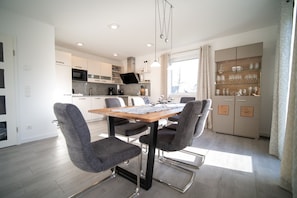 Una cocina moderna con armarios blancos, una mesa de comedor de madera y sillas grises.