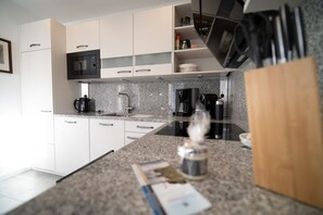 Una cocina moderna con armarios blancos, microondas integrado, cafetera y hervidor.