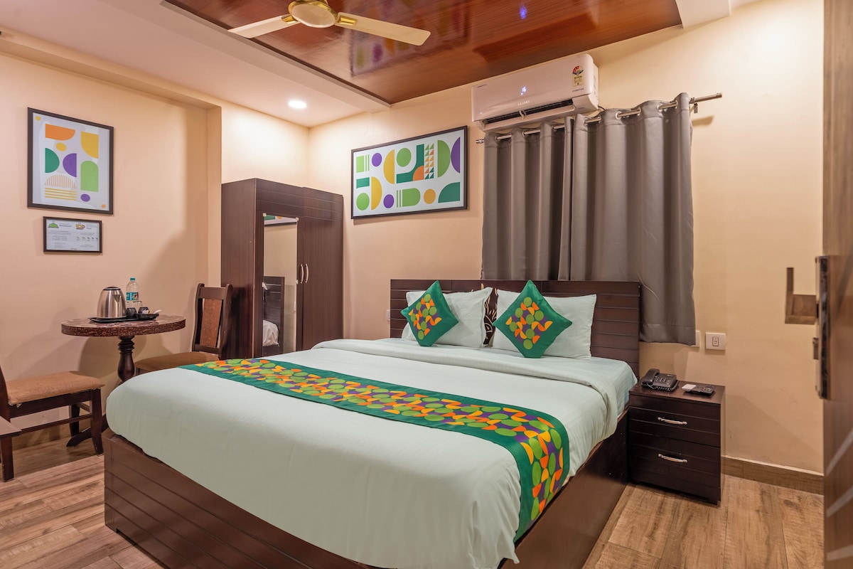 A hotel room with a bed, bedside table, chair, and artwork on the walls.