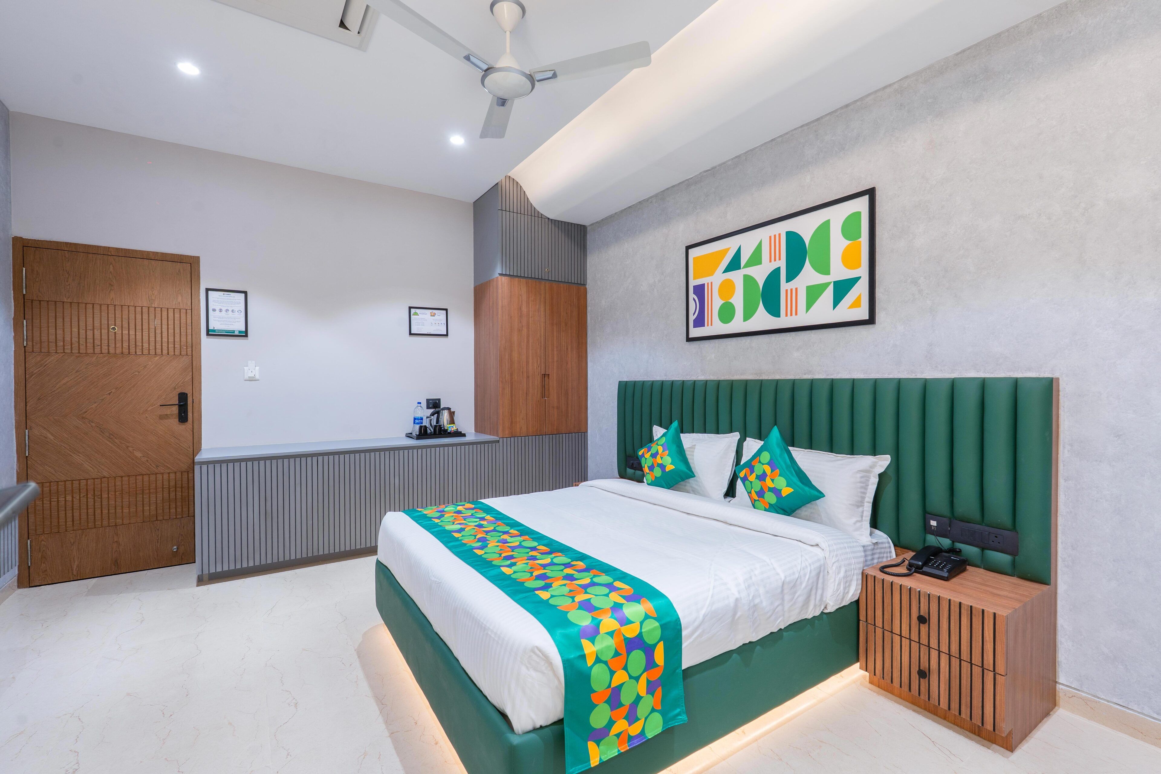 Habitació d'hotel moderna amb un llit gran, un panell del capçal verd, una petita taula de nit de fusta i un ventilador de sostre.