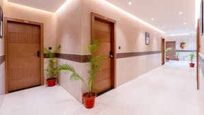 Un pasillo de hotel con puertas de madera, plantas en macetas y piso de mármol.