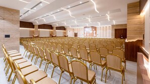 Un salón de conferencias con filas de sillas y una zona de escenario.