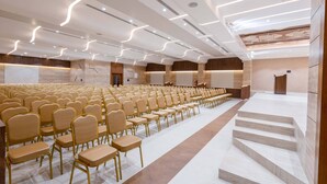 Un amplio salón de conferencias con filas de sillas, un escenario y una escalera.
