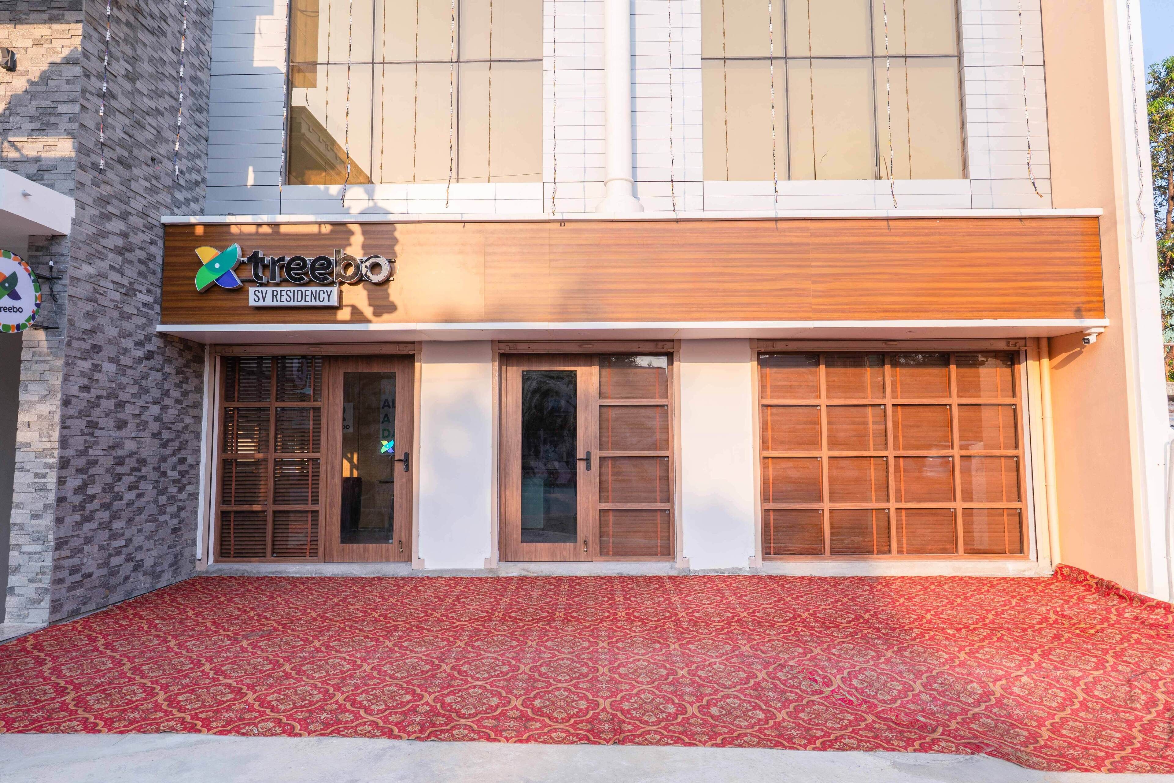 A building with a sign for 'treebo SV RESIDENCY' and a red patterned carpet in front.