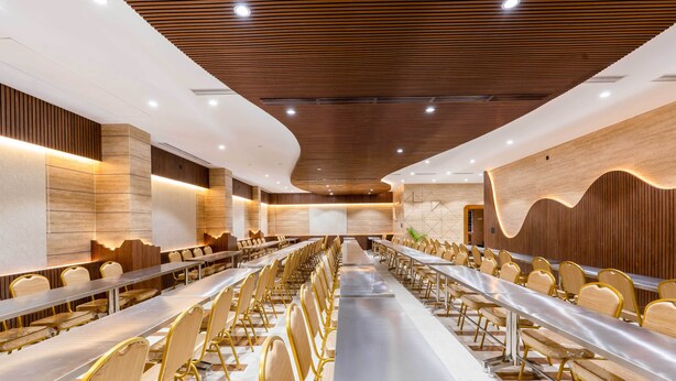 Una sala de conferencias moderna con mesas y sillas largas, paneles de madera en las paredes y techo de madera.