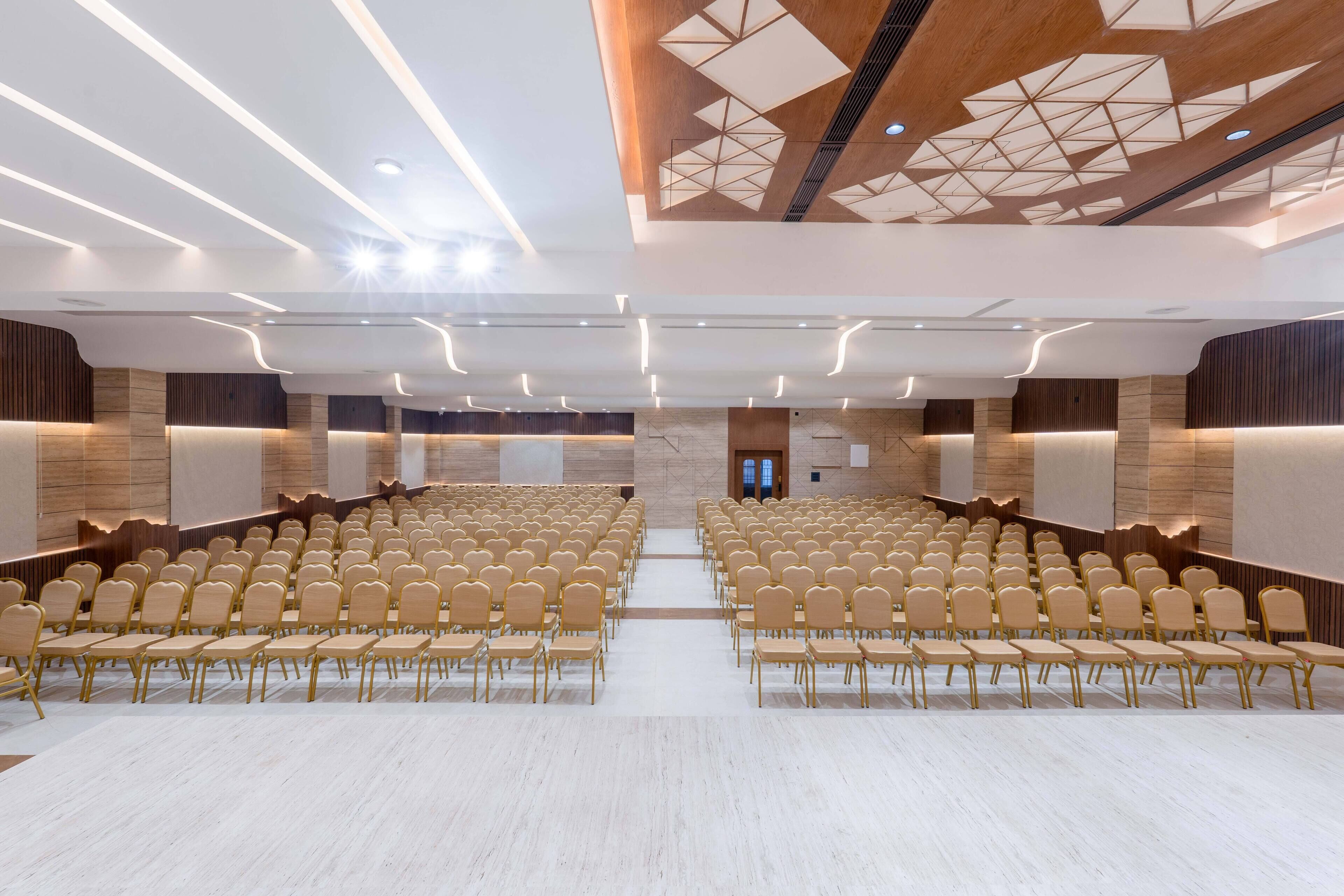 A spacious conference room with rows of chairs, a wooden ceiling with geometric patterns, and a central aisle.