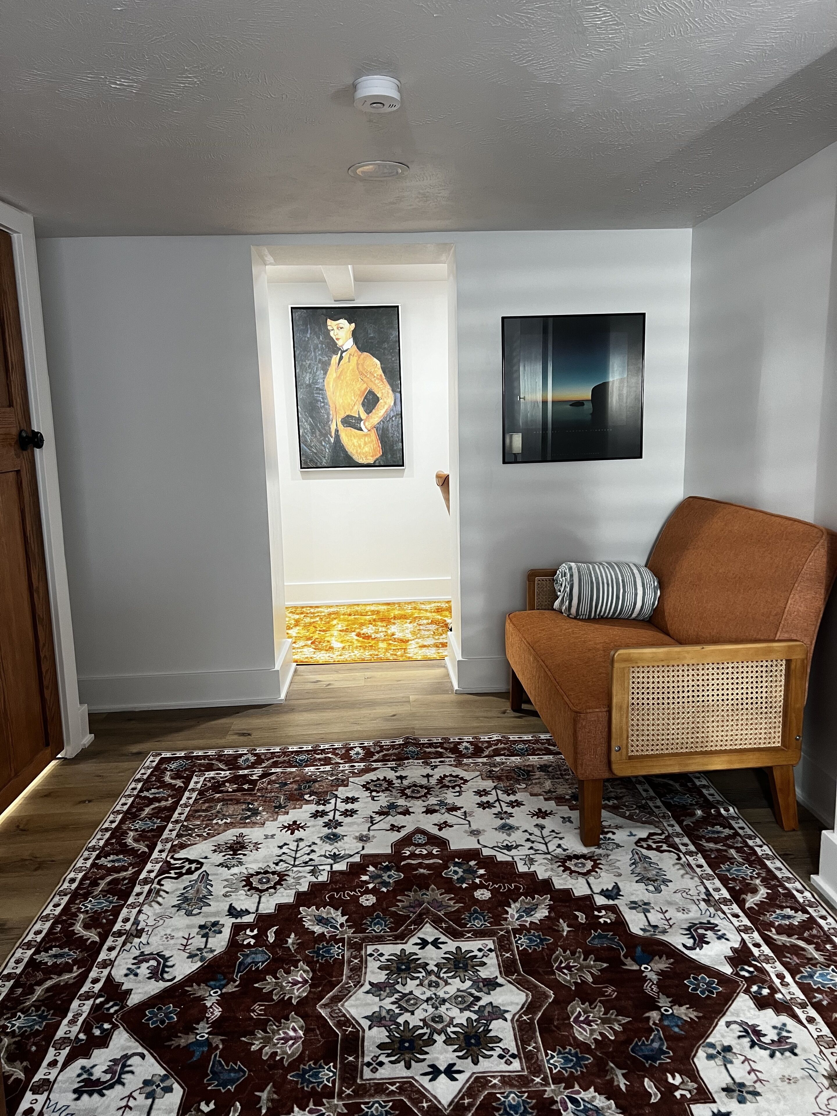 A living room with a patterned rug, a brown armchair, and two framed artworks on the wall.
