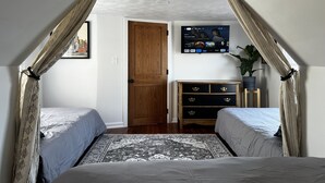 Ein Schlafzimmer mit zwei Betten, einem an der Wand montierten Fernseher, einem Holzschrank und einer Tür zu einem weiteren Raum.
