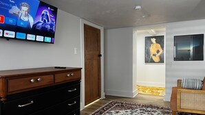 Ein modernes Wohnzimmer mit einem Flachbildfernseher, der einen Disney Bundle anzeigt, einer Holzkommode mit Schubladen, einem gemusterten Teppich und einem Bild an der Wand.