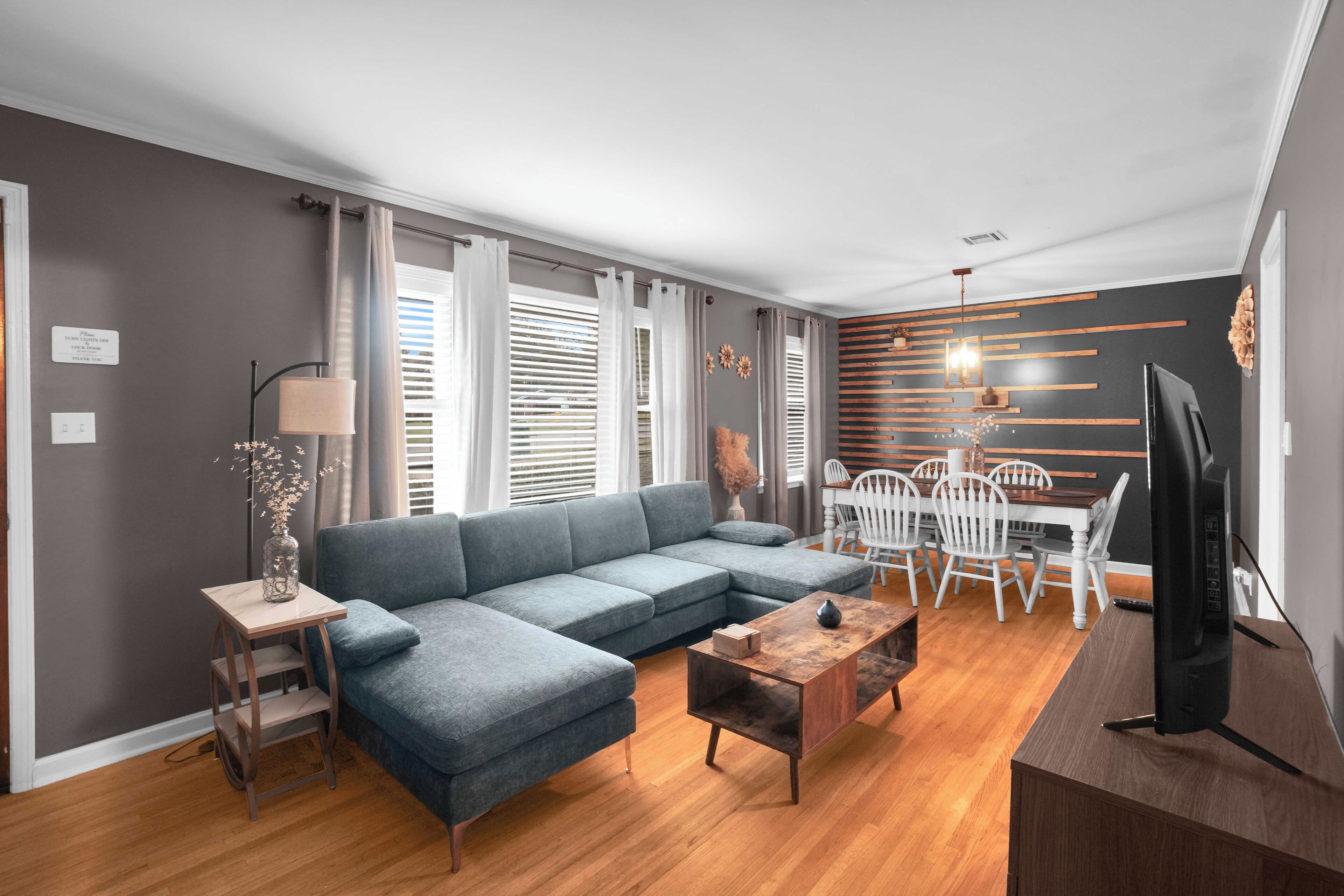 A modern living room with a sectional sofa, a dining table with chairs, a TV, and a wooden coffee table.