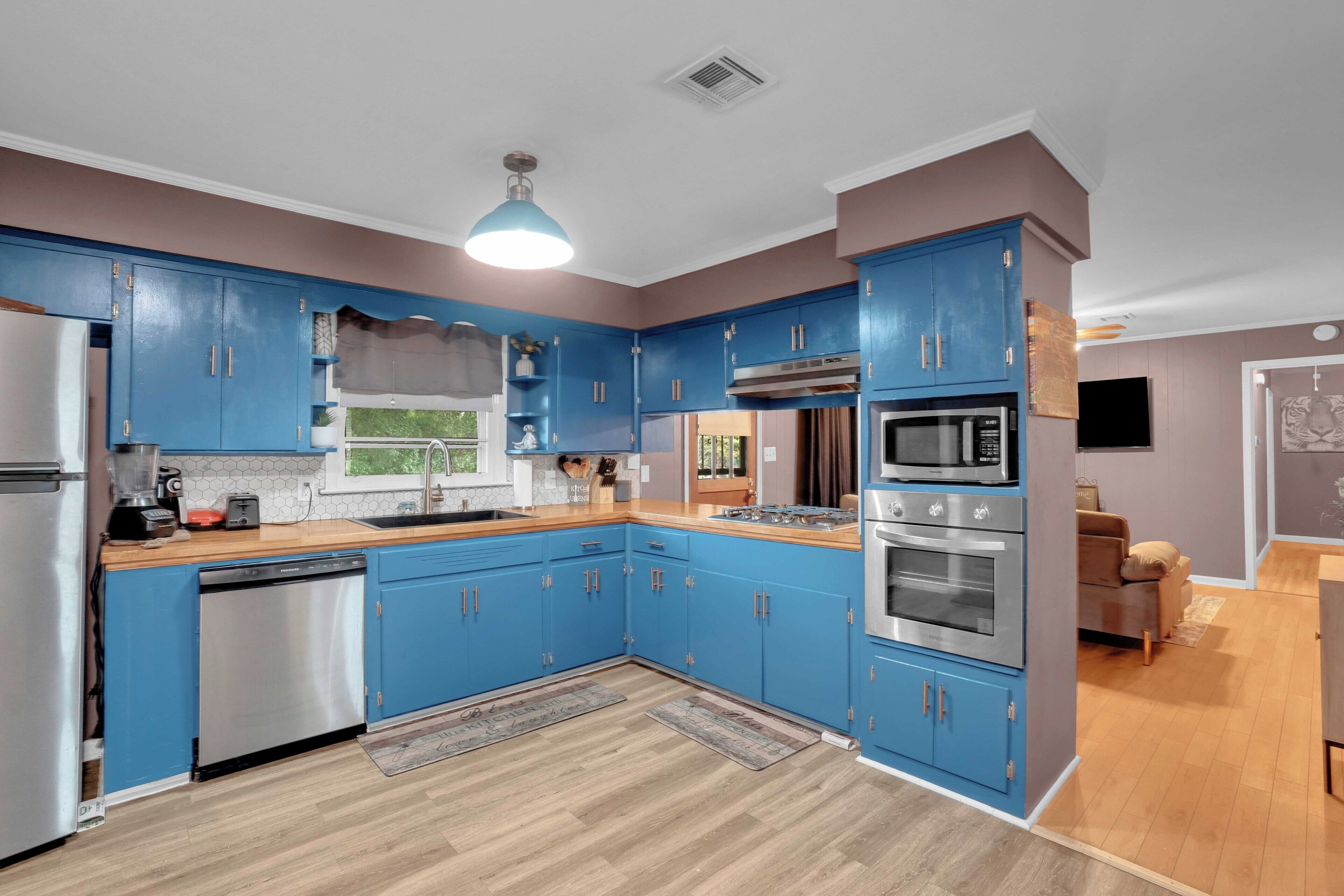 A modern kitchen with blue cabinets, stainless steel appliances, and a wooden countertop.