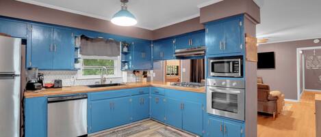 A modern kitchen with blue cabinets, stainless steel appliances, and a wooden countertop.