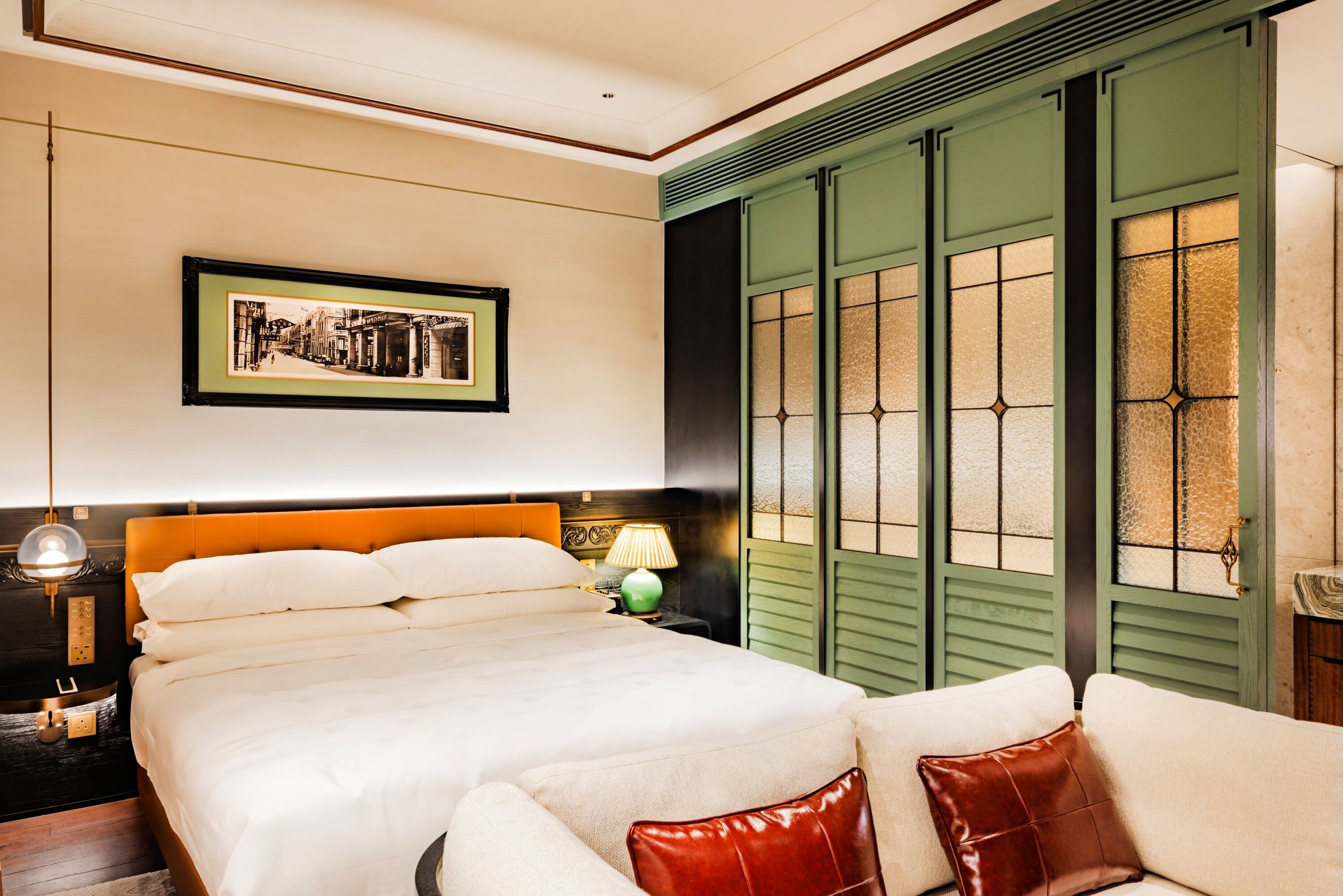 A neatly arranged bedroom with a large bed, a bedside table with a lamp, and a green door with glass panels.