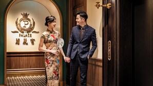A man and a woman holding hands in a hotel lobby with a sign reading "PALACE HOTEL" and a clock on the wall. - Hotel Central (Macau)
