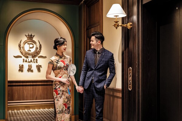 A man and a woman holding hands in a hotel lobby with a sign reading "PALACE HOTEL" and a clock on the wall. - Hotel Central (Macau)