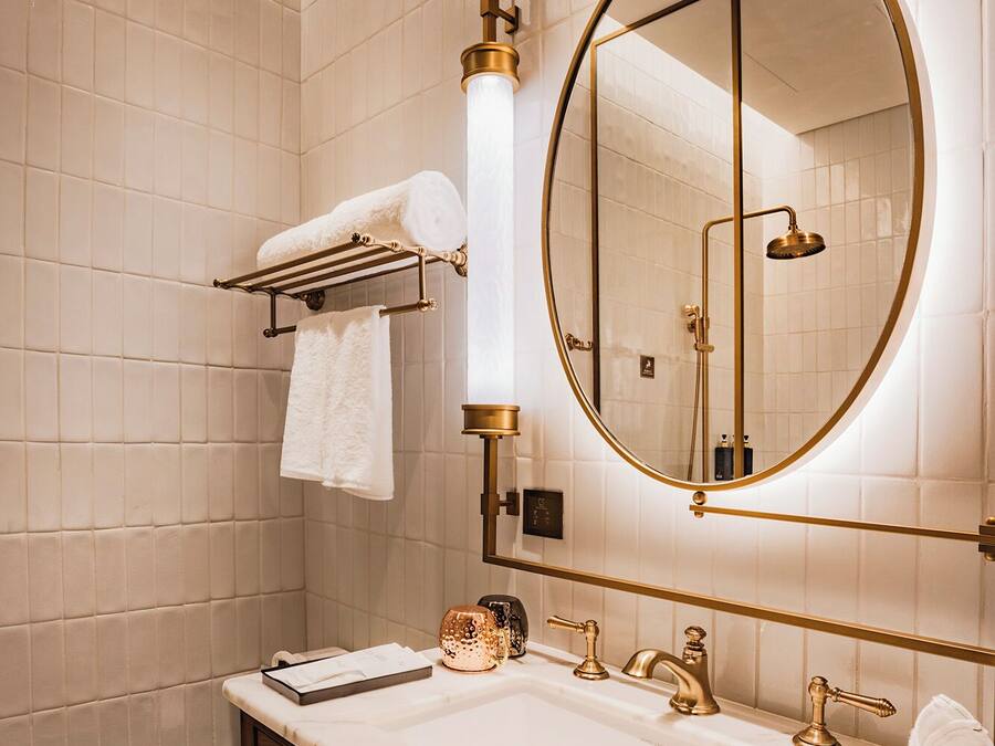 A bathroom with a marble sink, gold fixtures, a round mirror, and a towel rack.