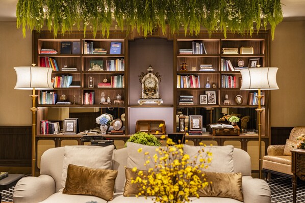 Una sala acogedora con un sofá, una estantería llena de libros y objetos decorativos, y un reloj grande.