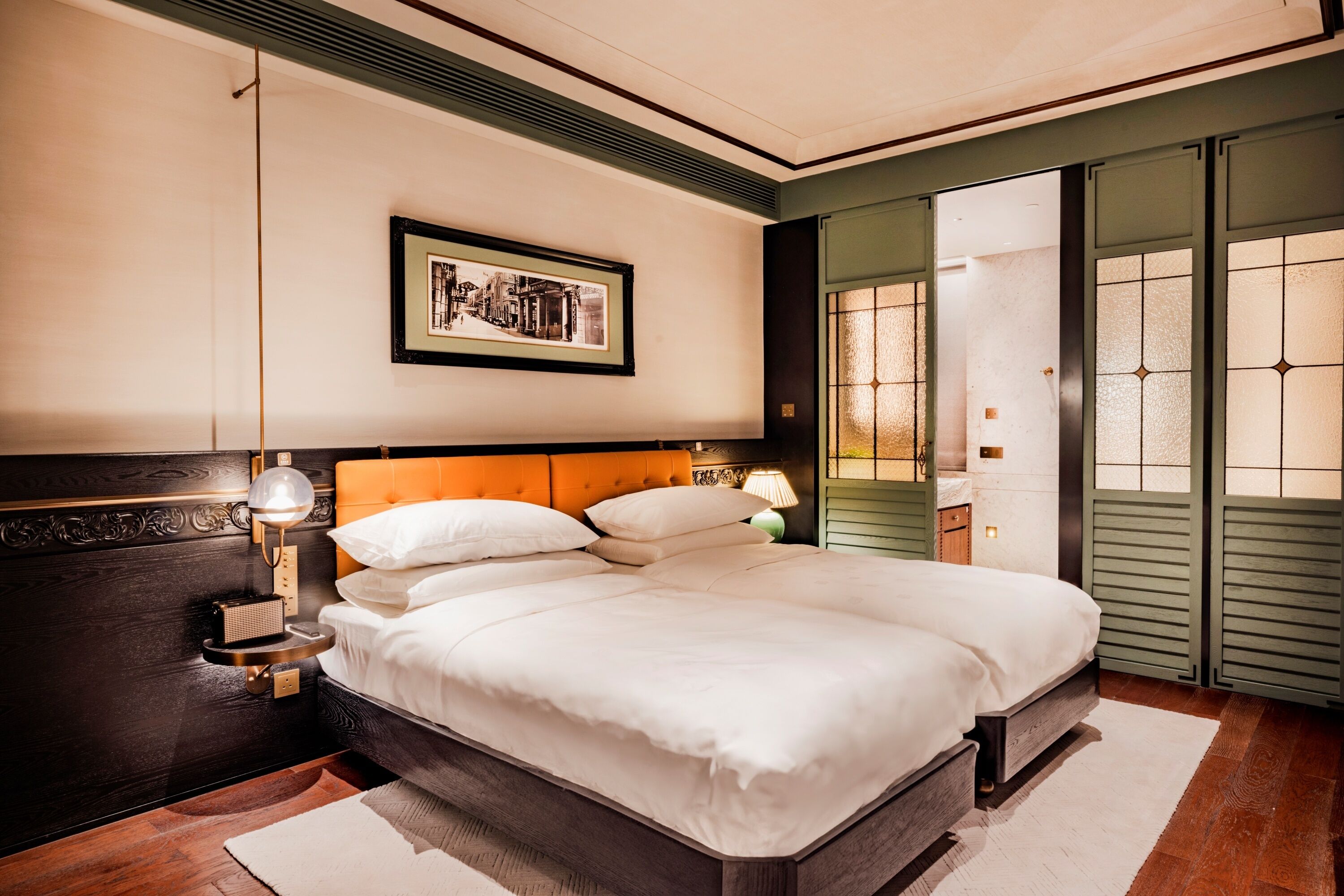 A neatly arranged bedroom with a large bed, a bedside table with a lamp, and a framed picture on the wall.