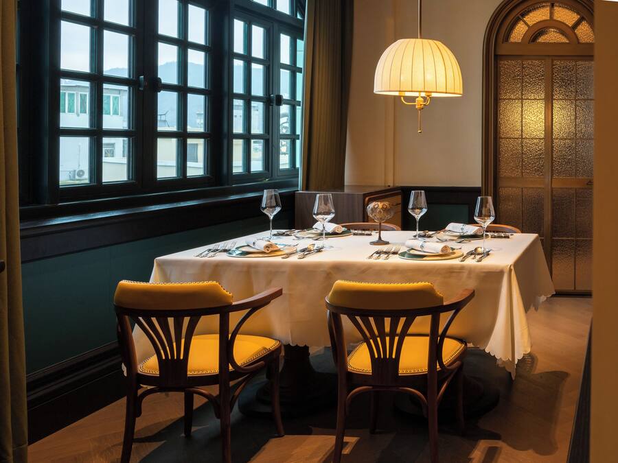 A dining area with a table set for two, a window with a view, and a lamp.