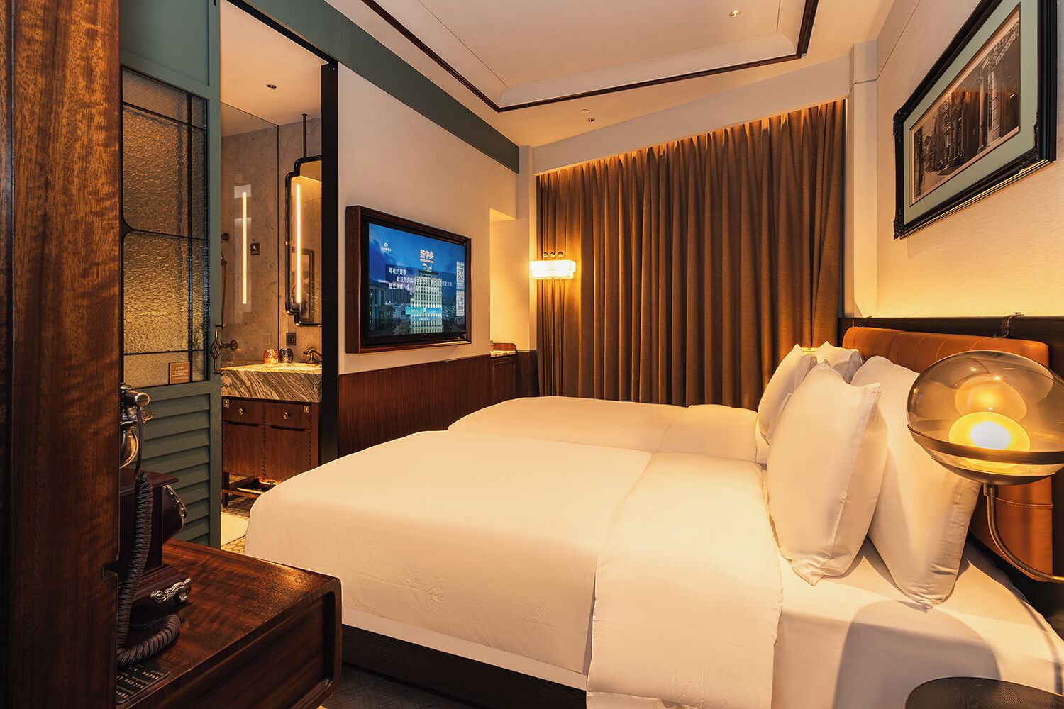 A hotel room with a large bed, a television, a desk with a telephone, and a mirror.