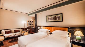 A hotel room with two beds, a sofa, a small table, a lamp, and a framed picture on the wall.