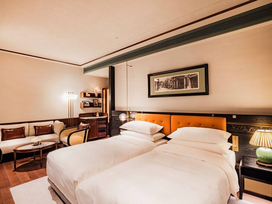 A hotel room with two beds, a sofa, a small table, a lamp, and a framed picture on the wall.