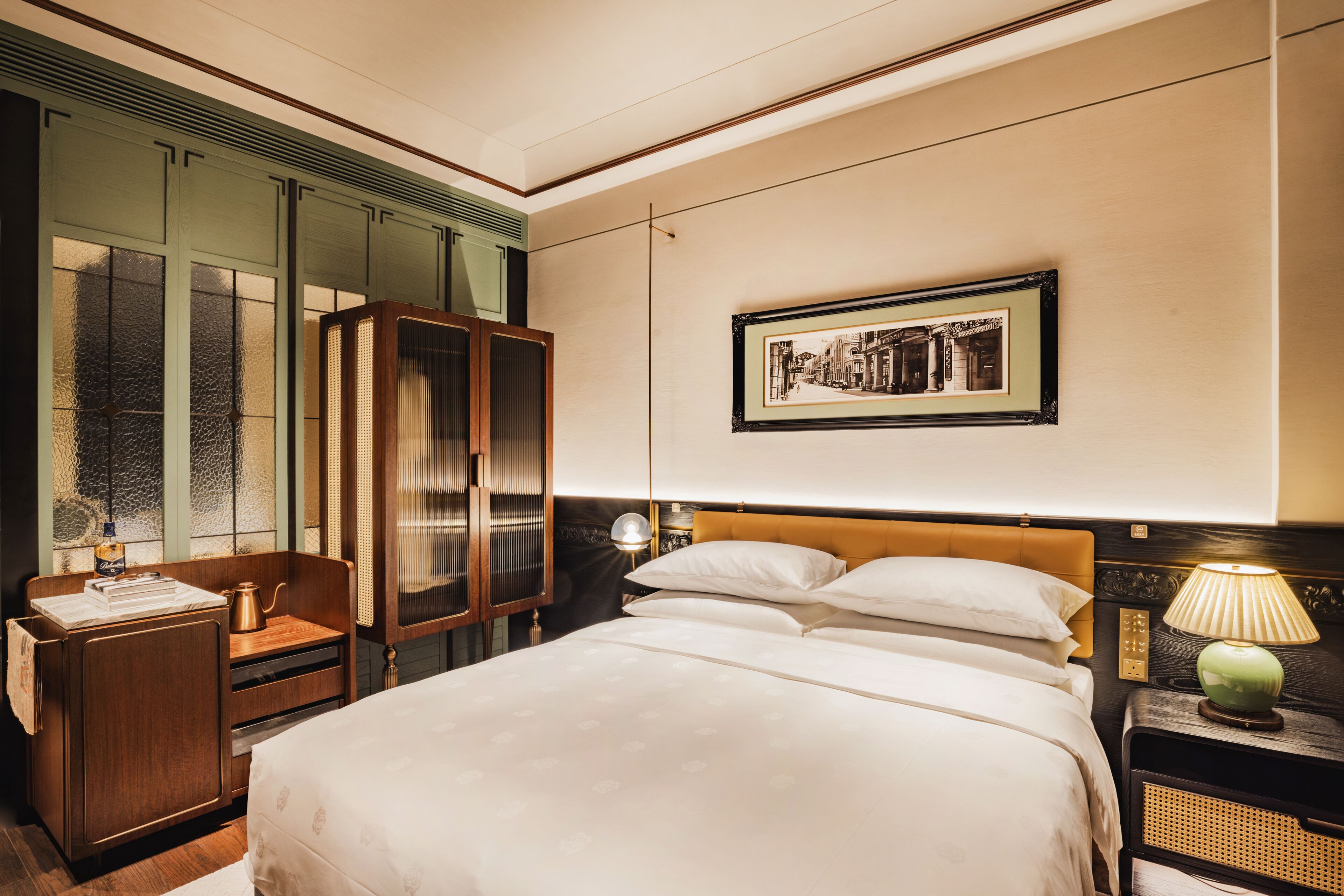 Een hotelkamer met een groot bed, een nachtkastje van hout met een lamp, een kledingkast en een lijst met een foto aan de muur.