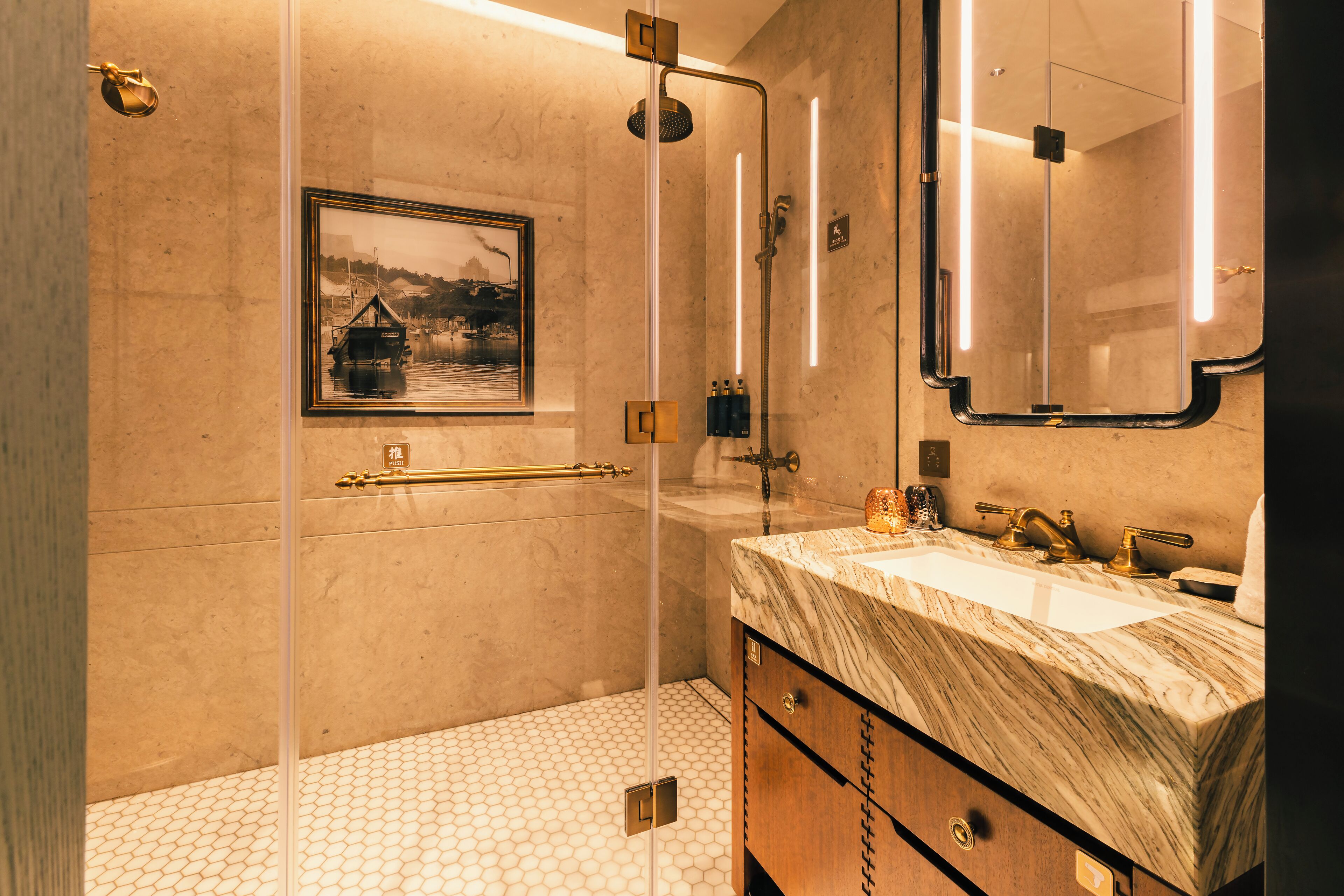 Un baño moderno con ducha de vidrio, lavamanos de mármol y un cuadro en la pared.